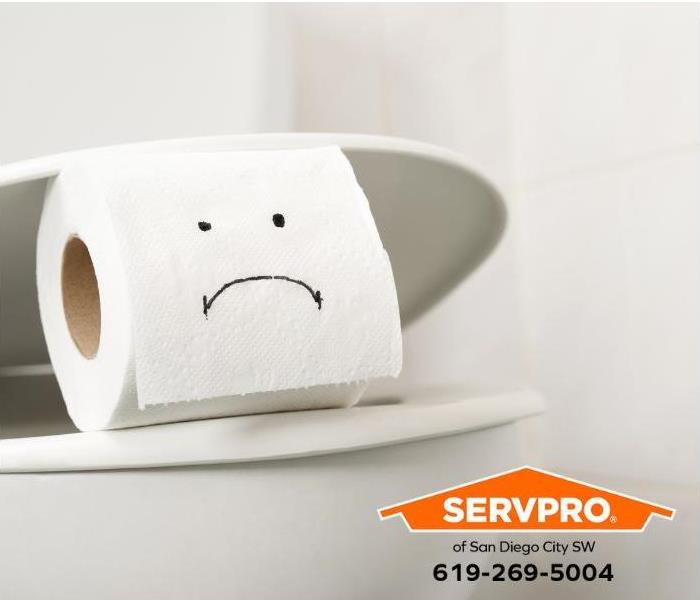 A frowning face is written on a roll of toilet paper that is sitting on a toilet.