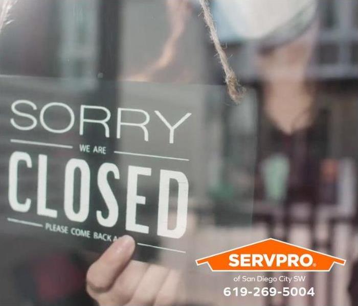 An employee places a “sorry we’re closed” sign on the front door of a commercial business.