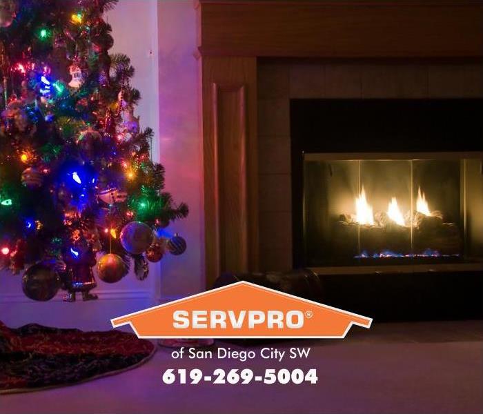 A fire is burning in a fireplace next to a Christmas tree decorated with ornaments and electric tree lights.